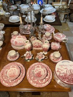 a table topped with lots of pink and white china dishes on top of a wooden table