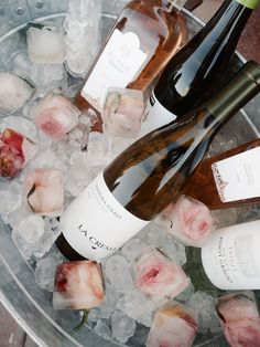 three bottles of wine sitting on top of an ice bucket filled with roses and ice cubes