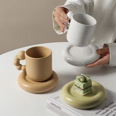 a woman holding a cup and saucer over a plate with a small house on it