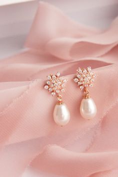 two pearls are attached to the back of a pair of earrings on a pink fabric