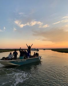 a group of people riding on top of a boat in the water at sunset with their arms up