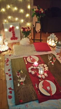 the table is set with red and white plates, silverware, candles and flowers