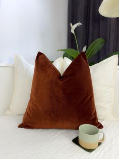 a brown pillow sitting on top of a bed next to a cup and saucer