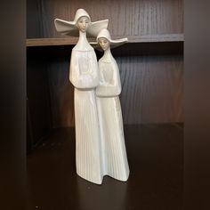 two white ceramic figurines are standing next to each other on a wooden shelf