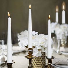 white candles are lit on a table with silverware and flowers in the vases