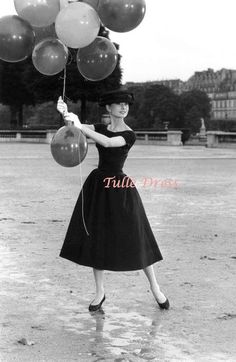 a woman in a black dress is holding some balloons