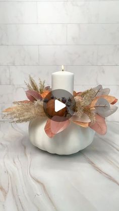 a white candle holder with flowers and leaves in it on a marble countertop next to a brick wall