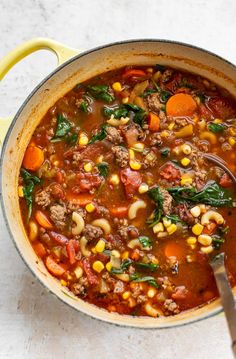 a pot full of soup with meat, beans and spinach on the side next to a spoon