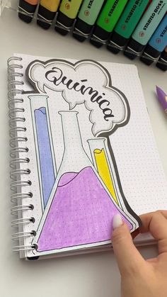 a hand is holding a notebook with colored crayons next to it