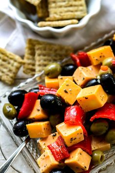 a glass dish filled with cheese and olives next to crackers on a table