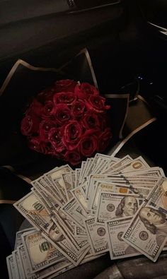 a bouquet of roses sitting on top of a pile of money next to a bunch of cash