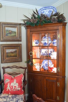 an old china cabinet with blue and white plates on the glass doors, next to a chair