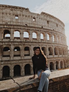 a woman sitting on top of a stone wall next to an old building with arches