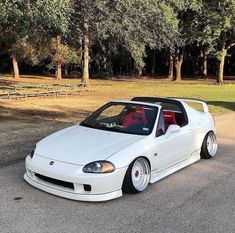 a white sports car parked in a parking lot next to trees and picnic tables with benches behind it