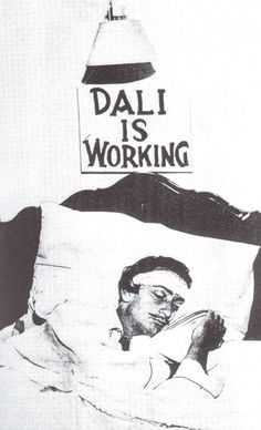 a black and white photo of a man laying in bed with dalii is working sign above him