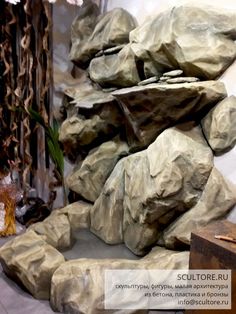 some rocks are stacked on top of each other in front of a wall with plants