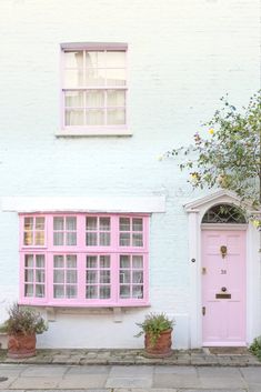 a pink door and window in front of a white brick building with potted plants