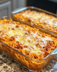 two glass casserole dishes filled with spaghetti and meat, sitting on a granite countertop