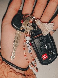 a person's hand holding several keys, including a car keychain and some beads