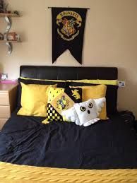 a harry potter themed bedroom with black and yellow bedding, hogwarts banner