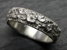 a silver ring with flowers on it sitting on top of a black surface and gray background