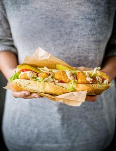 a person holding a sub sandwich in their hand with lettuce and chicken on it