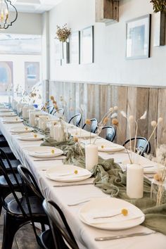 a long table is set with white plates and place settings