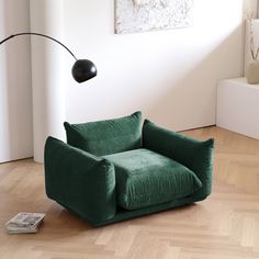 a green chair sitting on top of a hard wood floor next to a black lamp