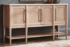 a sideboard with two doors and three drawers on it in front of a gray wall