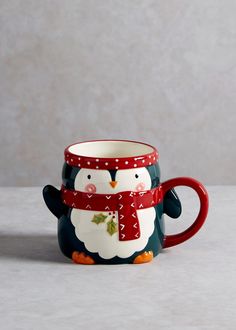 a penguin mug with a red scarf around it's neck and eyes, sitting on a white surface