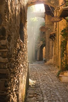 an alley way with cobblestones and stone buildings on both sides, in the sunlight