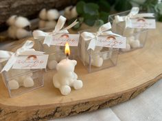 small white teddy bears sitting on top of a wooden table next to a lit candle