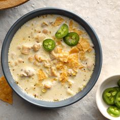 a bowl of soup with green peppers and tortilla chips next to it on a table