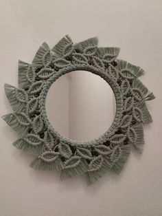 a circular mirror hanging on the wall next to a white wall with fringes around it