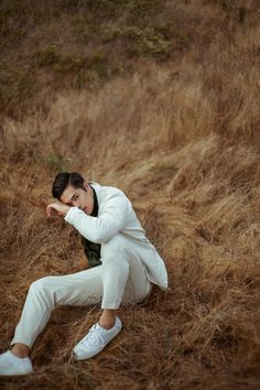 a man sitting on the ground with his arms behind his head, wearing white pants and sneakers