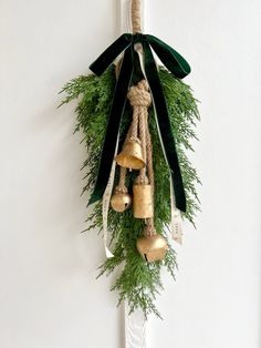 a bunch of bells hanging from a rope on a wall with greenery around it