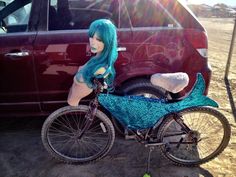 a woman with blue hair sitting next to a bike in front of a red car