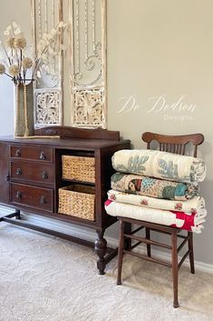 an old dresser and chair with pillows stacked on it next to a wall mounted mirror