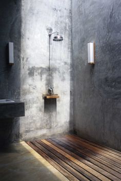 a bathroom with concrete walls and wooden flooring next to a sink, shower head and soap dispenser