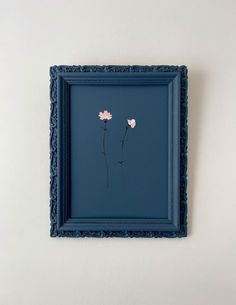 two pink flowers in a blue frame hanging on the wall