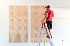 a man standing on a ladder in front of two wooden pegboards and working on the wall