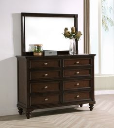 a dresser with a mirror on top of it and flowers in a vase next to it