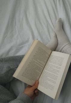 someone is reading a book in bed with their feet up on the pillow and socks