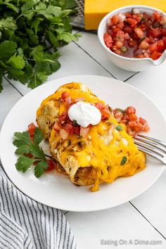 an enchilada on a plate with a fork and bowl of salsa in the background