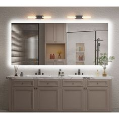 a bathroom vanity with two sinks and lights on the wall above it is illuminated by recessed lighting