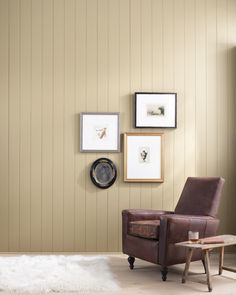 a brown chair sitting in front of a wall with pictures on the wall behind it