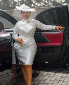 a woman in a white dress and hat standing next to the door of a car