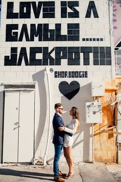 a man and woman standing in front of a wall with words on it that say love is a game