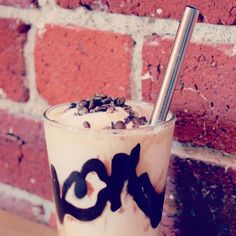 an iced drink with whipped cream and chocolate sprinkles on the rim next to a brick wall