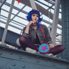 a woman with blue hair sitting on top of a metal structure holding a handbag